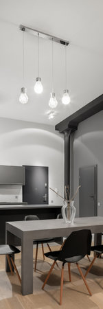 Vertical panorama of dark, gray kitchen with modern dining table with black chairs under stylish ceiling lamps in loft style apartmentの写真素材