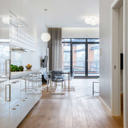 Modern kitchen with white furniture, modern dining area and window doors to balconyの写真素材