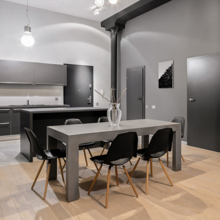 Big, modern and gray dining table with six black chairs in open kitchen in new loft apartment with dark doorsの写真素材