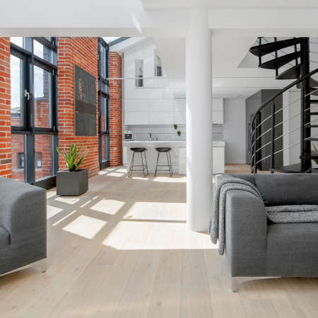 Modern loft apartment in white with red brick on the walls, big windows, black stairs and kitchen open to living roomの写真素材