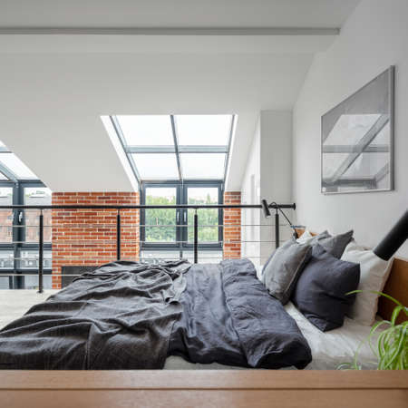 Stylish bedroom with big, comfortable bed on mezzanine in loft style apartment with big windows and brick on the wallの写真素材