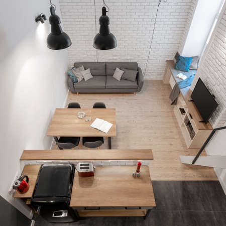 Top view of small and stylish studio apartment with brick walls, wooden floor and furniture and kitchen, living room and dining area in one roomの写真素材