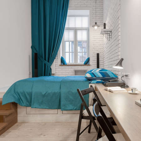 Modern bedroom with long desk for two, comfortable bed and big window with decorative curtain in loft apartmentの写真素材