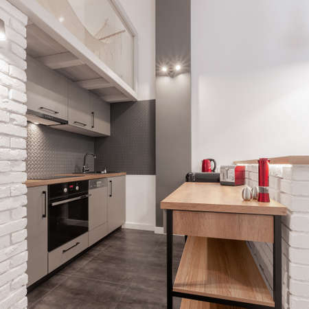 Small and functional kitchen with stylish gray furniture, wooden countertops and shelves and white brick on wallsの写真素材