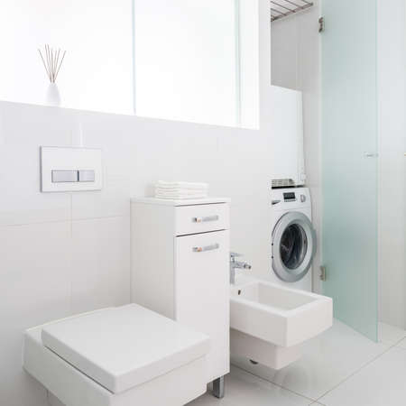 Simple and bright bathroom in white with cubic toilet and bidet and washing machine behind frosted glass doorsの写真素材