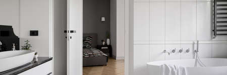 Panorama of luxury white bathroom with elegant bathtub next to master bedroom with big and comfortable bedの写真素材