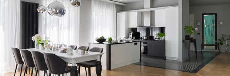Panorama of fancy black and white kitchen with long, decorated dining table with gray chairsの写真素材