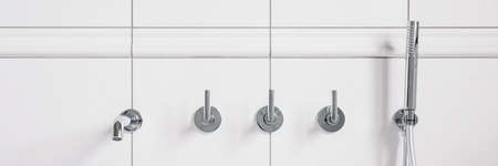 Panorama of elegant and fancy, silver wall mounted bathtub faucet and shower and wall in simple white tilesの写真素材