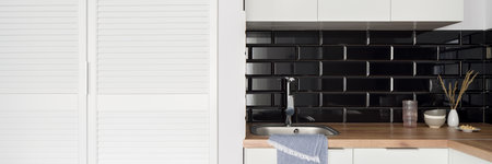 Panorama of small sink in white kitchen with wardrobe, wooden countertop and black brick style wall tilesの写真素材