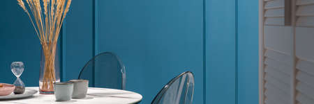 Panorama of nice and delicate decorations on dining table with marble countertop and plastic chairs in room with amazing teal blue wall with moldingの写真素材