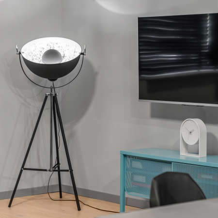 Stylish and industrial, black lamp on tripod in room with big television screen above blue sideboard with white clockの写真素材