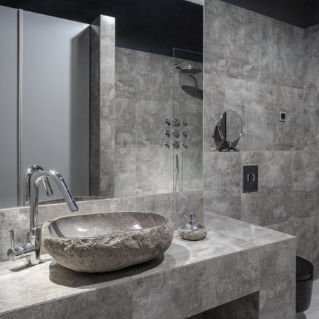 Dark and modern bathroom with gray wall tiles, stone like washbasin with new silver tap and big mirrorの写真素材