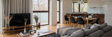 Panorama of bright apartment with big windows and spacious living room with television screen open to kitchen with dining tableの写真素材