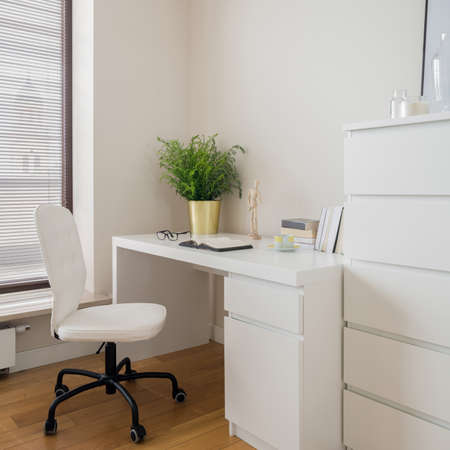 Functional home office room with simple white desk, white chest of drawers and black and white chairの写真素材