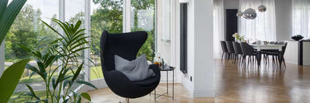 Panorama of spacious apartment with window wall and relax area with black chairの写真素材