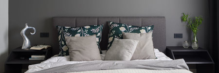 Panorama of elegant bedroom with comfortable bed with gray, quilted headboard, two black and modern bedside table with decorations and stylish gray wallの写真素材