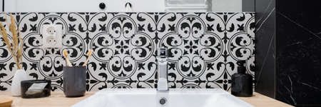 Panoramic close-up on simple bathroom washbasin with silver tap in wooden countertop and with decorative, patterned wall tilesの写真素材