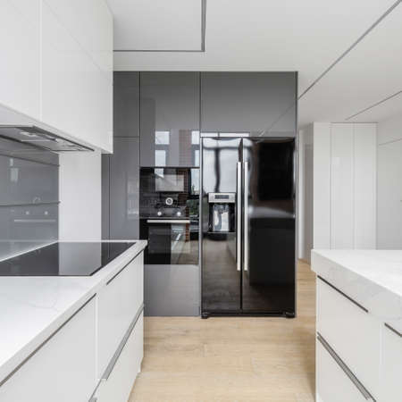 Exclusive kitchen with white furniture and countertops and gray backsplash tiles and big black fridge next to oven and microwaveの写真素材