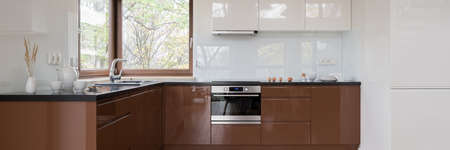 Spacious kitchen with white and brown cupboards and drawers, black countertops and windowの写真素材