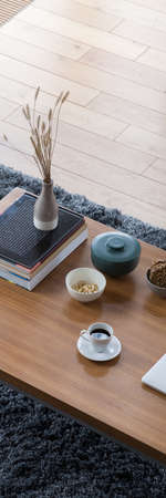 Panoramic top view on wooden and simple coffee table with books, vase, bowls and decorative containers and white cup of coffeeの写真素材