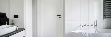 Panorama of luxury black and white bathroom with freestanding bathtub, stylish washbasin and white doors with black handleの写真素材