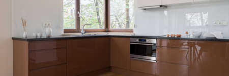 Panorama of spacious and modern kitchen with brown cupboards and drawers, black countertops and windowの写真素材