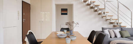 Panorama of wooden dining table with black chairs in spacious, two-story apartment interior with modern stairsの写真素材