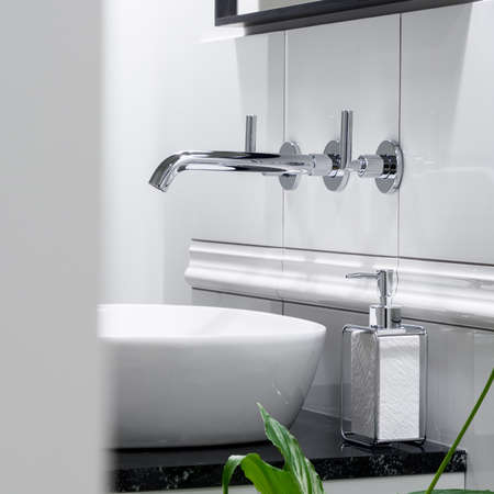 Close-up on stylish, silver wall mounted faucet in washbasin in elegant bathroom with white tiles and mirror in black frameの写真素材