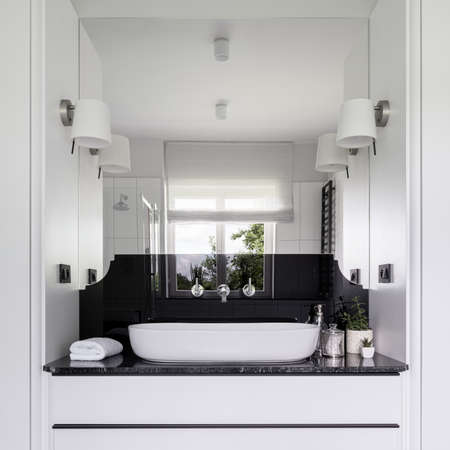 Elegant black and white bathroom with big mirror, elegant washbasin with nice silver taps, black countertop and white drawersの写真素材