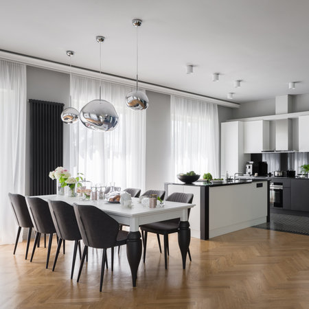 Fancy black and white kitchen with long, nice decorated dining table with gray chairs under stylish silver pendant lampsの写真素材