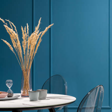 Close-up on nice and delicate decorations on stylish table with marble countertop and plastic chairs in dining room with amazing teal blue wall with moldingの写真素材