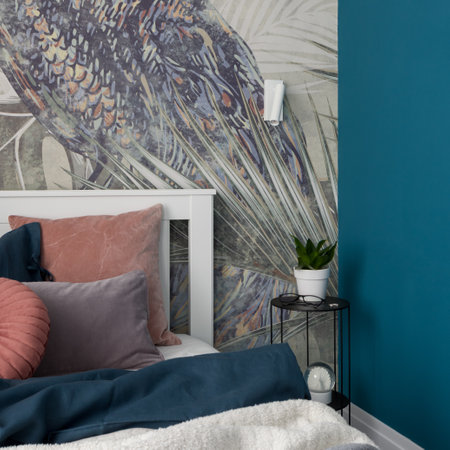 Close-up on comfortable bed with nice bedclothes and simple black bedside table with decorations in charming bedroom with stylish wallpaperの写真素材