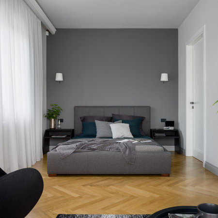 Stylish and simple bedroom with comfortable, double bed with gray upholstered frame, wooden floor and long, white window curtainsの写真素材