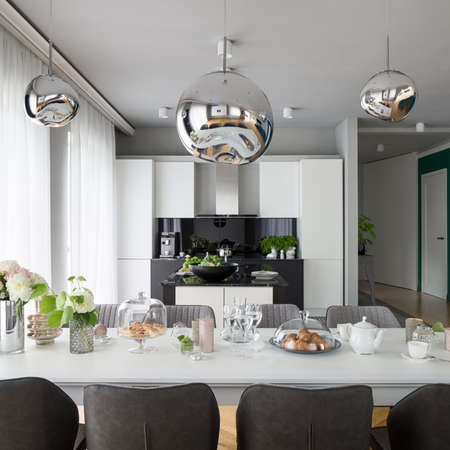 Beautiful decorated dining table with stylish chairs, under silver chandelier in spacious and elegant kitchenの写真素材