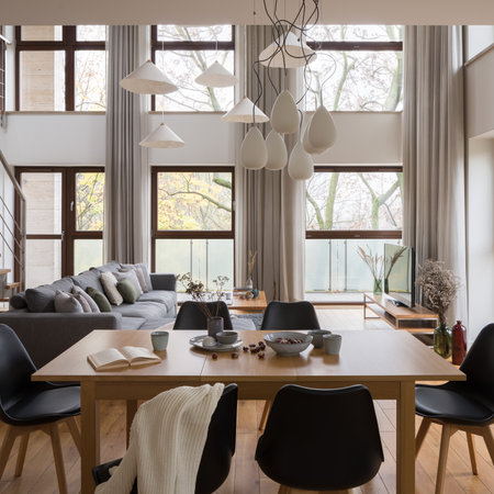 Wooden dining table with black chairs and stylish decorations in spacious living room with big windowsの写真素材