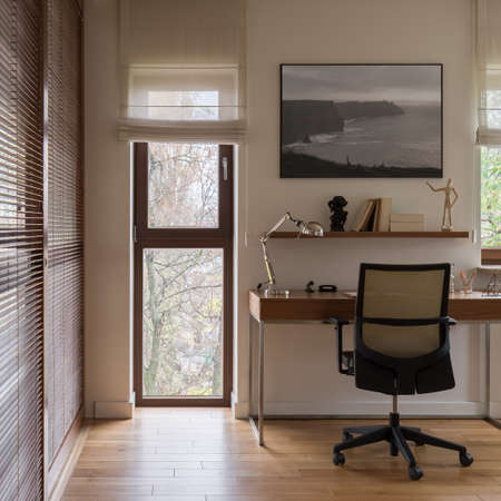 Wood decor in elegant and comfortable home office room with window walls with wooden shutters, wooden floor, wooden desk and comfortable chairの写真素材