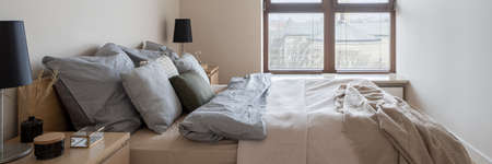 Panorama of beautiful bedroom with comfortable bed with nice bedclothes and big windowの写真素材