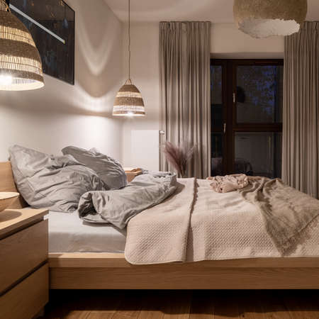 Night in comfortable and nice decorated bedroom with big bed, rattan lamps, beige colors and natural textilesの写真素材