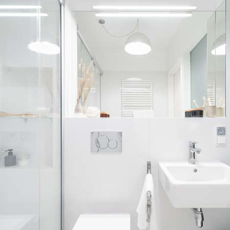 Small and stylish bathroom in white with shower, big mirror, classic washbasin and decorative ceiling lightの写真素材