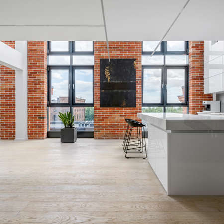 Big windows and brick walls in modern kitchen with white furniture and wooden floorの写真素材