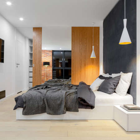 Comfortable big bed with upholstered wall in stylish and spacious bedroom with wardrobe with wooden door and mirrorの写真素材