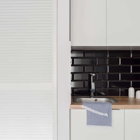 Close -up on small kitchen sink with black rectangular backsplash tiles next to white wardrobeの写真素材