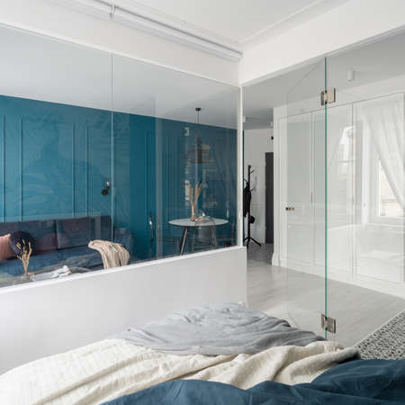 Elegant and small studio apartment with bedroom behind glass wall with view to living room with blue wallの写真素材