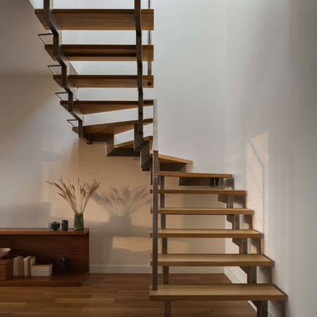 Close-up on stylish wooden stairs with modern silver railing in home interior with nice and warm sunlightの写真素材