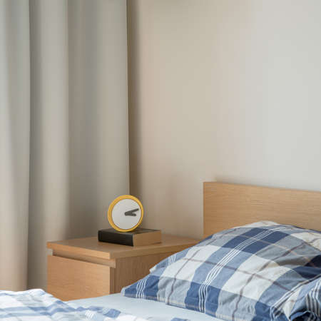 Close-up on yellow clock on wooden bedside table in bright bedroomの写真素材