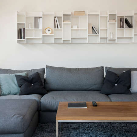 Modern white shelf with books and decorations above comfortable, gray corner sofaの写真素材