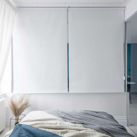 Small and stylish bedroom with white window blinds on wall and glass doorsの写真素材