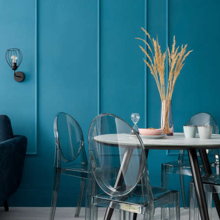 New dining table with decorations, marble style countertop with modern, four transparent chairs in elegant room with teal blue wall with moldingの写真素材