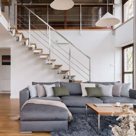 Big, comfortable corner sofa in spacious living room with modern stairs in two-storey loft apartmentの写真素材