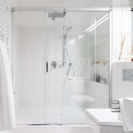 Spacious shower behind glass sliding doors in simple bathroom with white tilesの写真素材